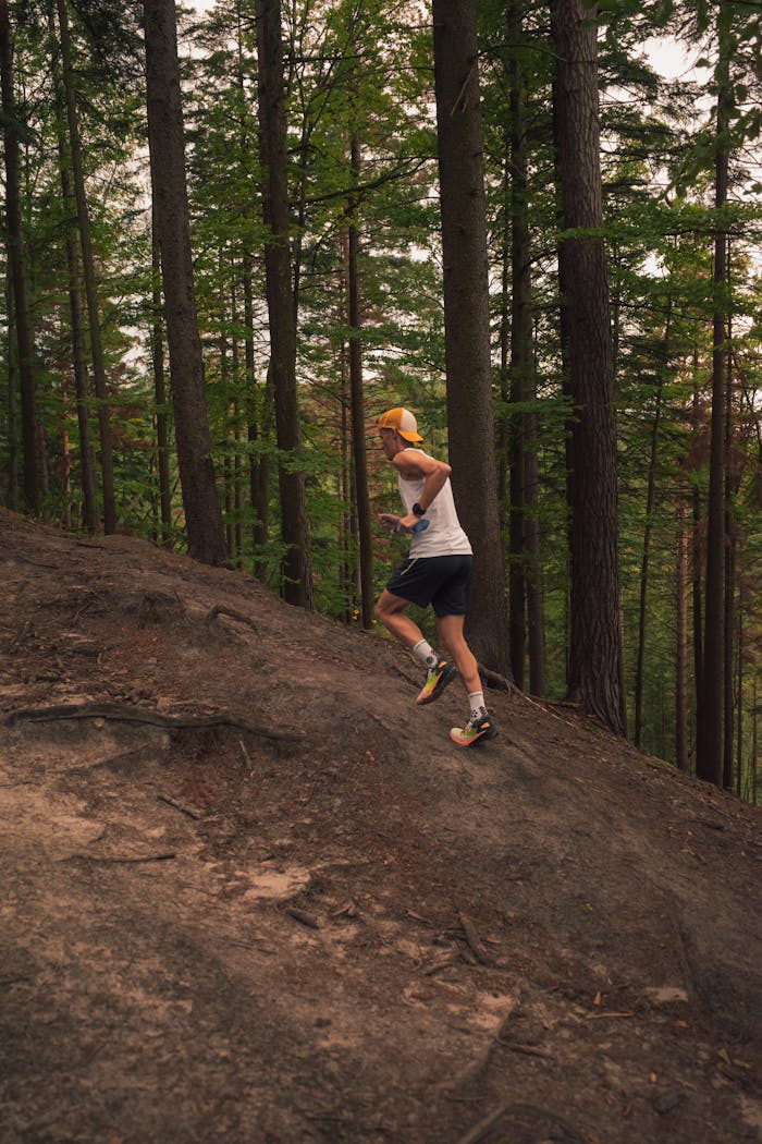 Athlete running uphill on a forest trail wearing athletic gear during summer.